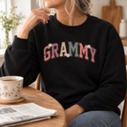 Woman wearing the black Grammy Retro Daisy Sweatshirt at a kitchen table