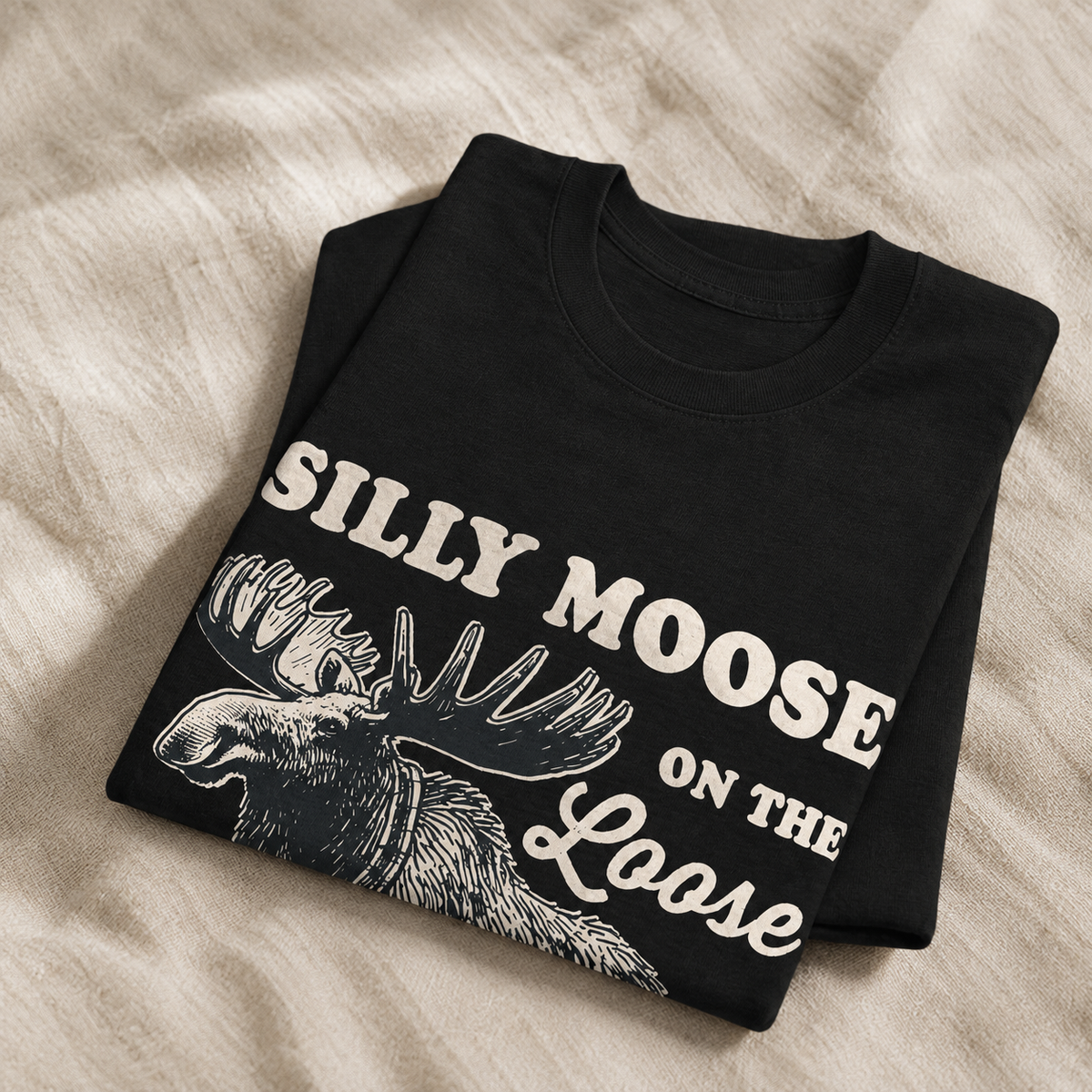 Folded black t-shirt with a soft matte Silly Moose print on linen